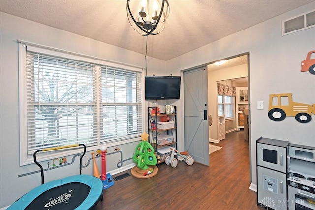 game room with a wealth of natural light, dark hardwood / wood-style flooring, a textured ceiling, and an inviting chandelier