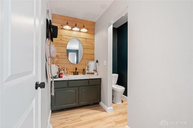 bathroom featuring vanity, hardwood / wood-style floors, wooden walls, and toilet