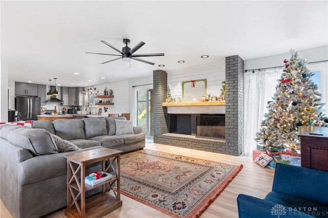 living room with ceiling fan, plenty of natural light, a fireplace, and light hardwood / wood-style flooring