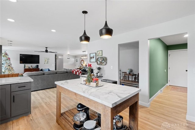 kitchen with light stone counters, pendant lighting, light hardwood / wood-style flooring, and ceiling fan