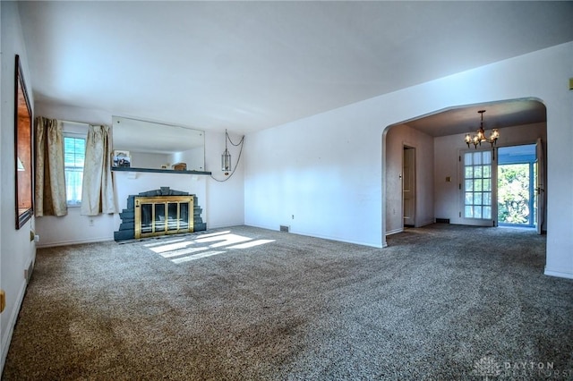 unfurnished living room with a wealth of natural light, carpet floors, and a notable chandelier