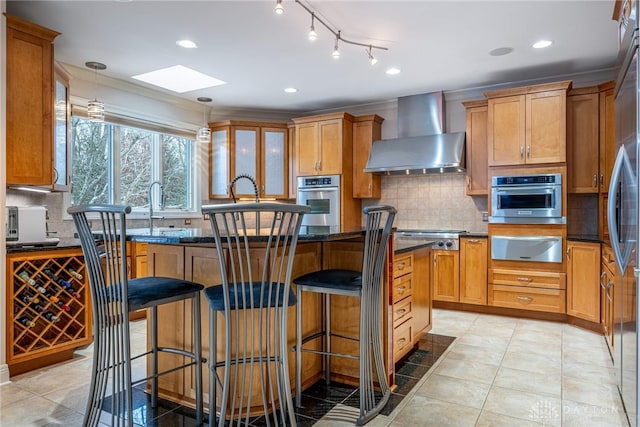 kitchen with appliances with stainless steel finishes, a center island, hanging light fixtures, and wall chimney range hood