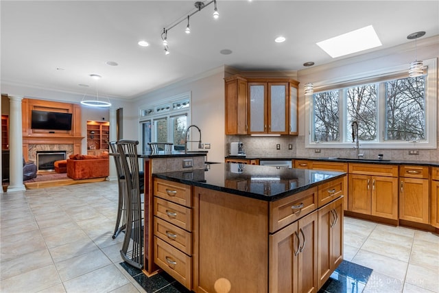 kitchen with dark stone counters, sink, hanging light fixtures, crown molding, and an island with sink