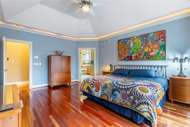 bedroom with ceiling fan, a raised ceiling, ensuite bathroom, wood-type flooring, and lofted ceiling