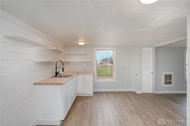 kitchen featuring wooden walls, butcher block countertops, sink, white cabinets, and a textured ceiling