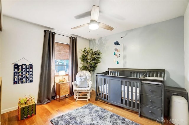 bedroom with hardwood / wood-style flooring, ceiling fan, and a crib