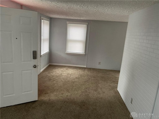 carpeted empty room featuring baseboards, brick wall, and a textured ceiling