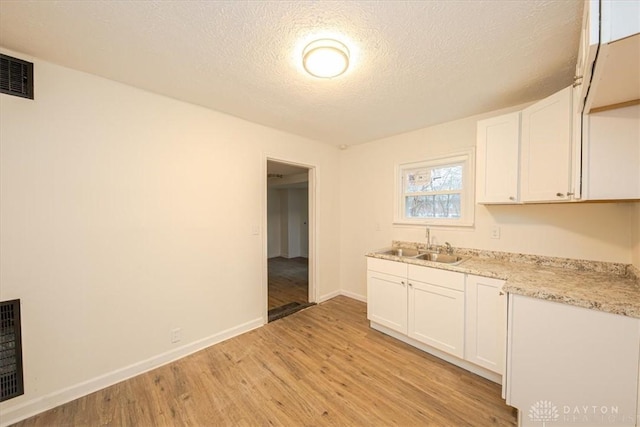 kitchen with sink, a textured ceiling, light hardwood / wood-style flooring, and white cabinets