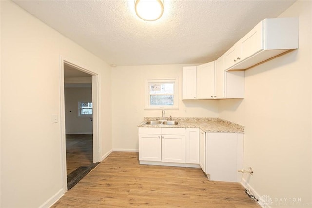 kitchen featuring white cabinetry, sink, light hardwood / wood-style floors, and a textured ceiling