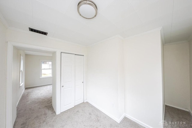 unfurnished bedroom with crown molding, light carpet, and a closet