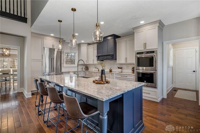 kitchen with sink, stainless steel appliances, an island with sink, pendant lighting, and a breakfast bar