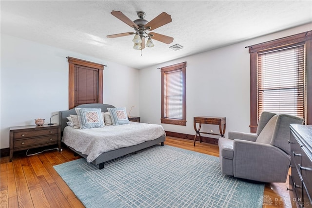 bedroom with multiple windows, ceiling fan, hardwood / wood-style floors, and a textured ceiling