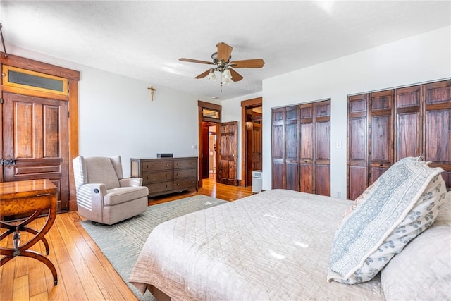 bedroom featuring light hardwood / wood-style floors, ceiling fan, and multiple closets