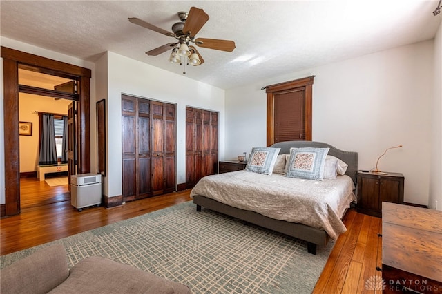 bedroom featuring hardwood / wood-style flooring, ceiling fan, a textured ceiling, and two closets