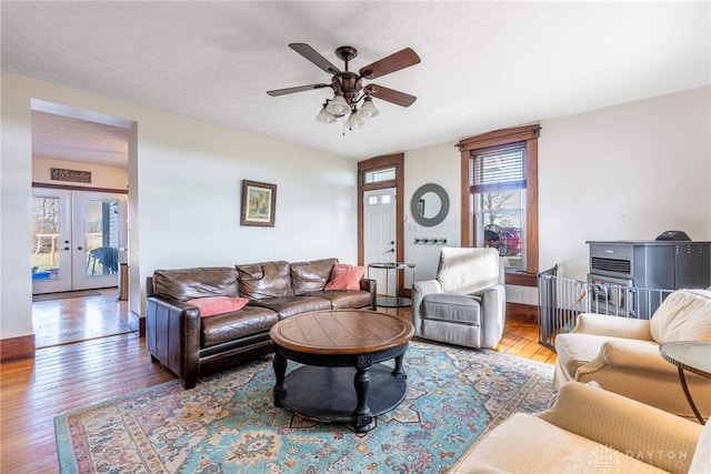 living room featuring ceiling fan, french doors, light hardwood / wood-style floors, and a textured ceiling