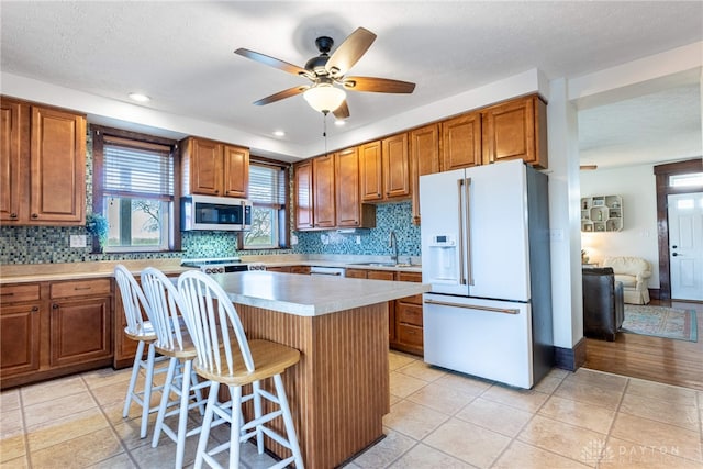 kitchen with white appliances, a kitchen breakfast bar, sink, ceiling fan, and a kitchen island