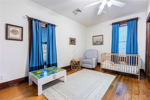 bedroom with ceiling fan, a nursery area, and wood-type flooring