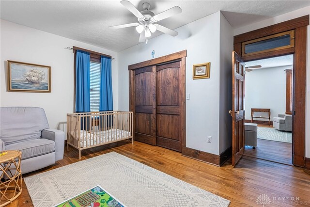 bedroom with a crib, hardwood / wood-style floors, and ceiling fan