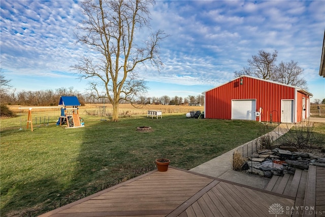 view of yard featuring an outdoor structure, a wooden deck, a rural view, a playground, and a garage