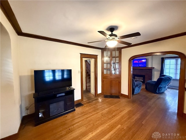 living room with hardwood / wood-style flooring, ceiling fan, ornamental molding, and a brick fireplace