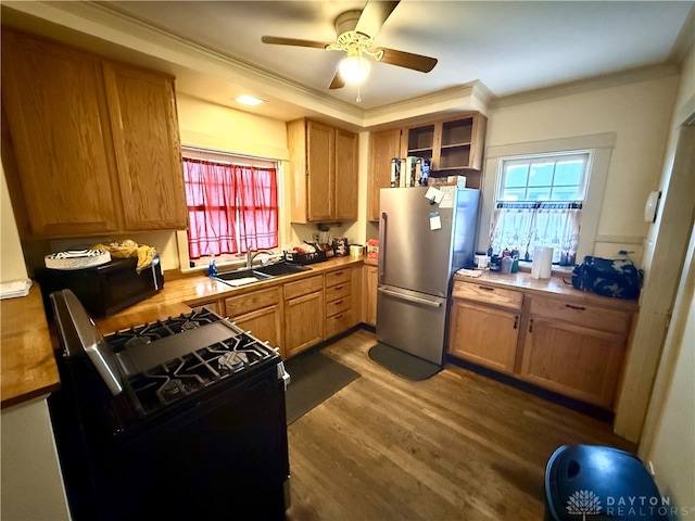 kitchen with gas stove, stainless steel refrigerator, sink, dark hardwood / wood-style floors, and ornamental molding