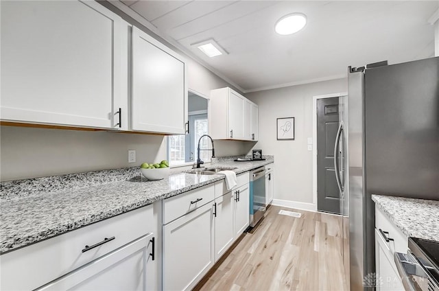 kitchen featuring light stone countertops, sink, stainless steel appliances, light hardwood / wood-style floors, and white cabinets