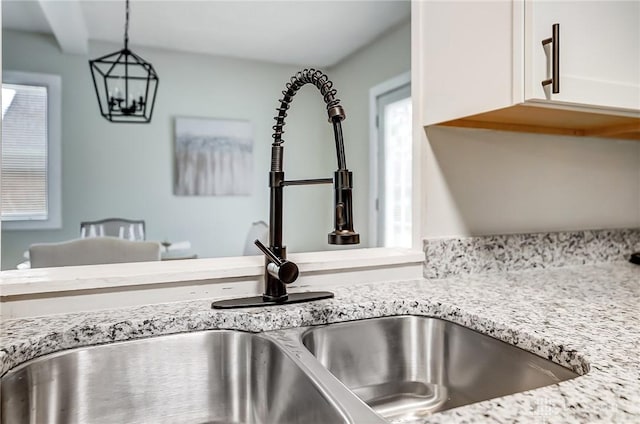 room details featuring pendant lighting, sink, white cabinetry, and light stone counters