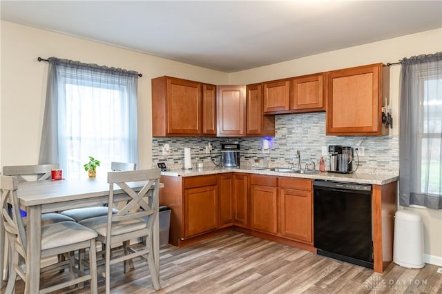 kitchen with black dishwasher, brown cabinets, backsplash, light wood-style floors, and a sink