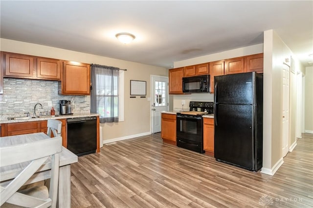 kitchen with brown cabinets, light wood finished floors, light countertops, a sink, and black appliances