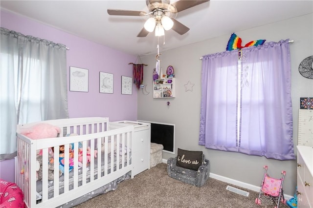 carpeted bedroom featuring ceiling fan and a nursery area