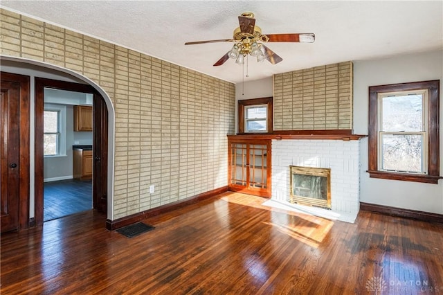 unfurnished living room featuring dark hardwood / wood-style floors, a brick fireplace, ceiling fan, and a healthy amount of sunlight