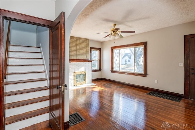 unfurnished living room featuring hardwood / wood-style flooring, ceiling fan, a fireplace, and a textured ceiling