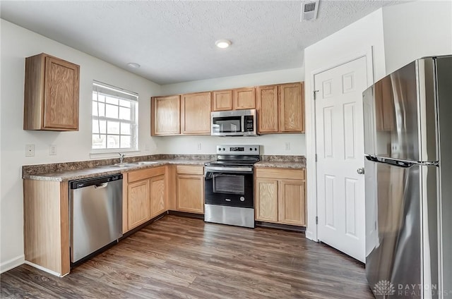 kitchen with stainless steel appliances, dark hardwood / wood-style floors, light brown cabinetry, a textured ceiling, and sink