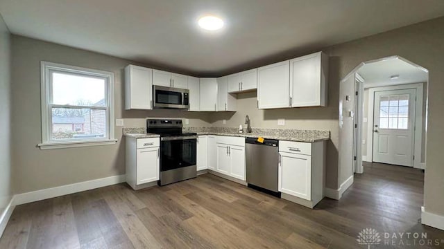 kitchen featuring light stone countertops, stainless steel appliances, dark wood-type flooring, sink, and white cabinets