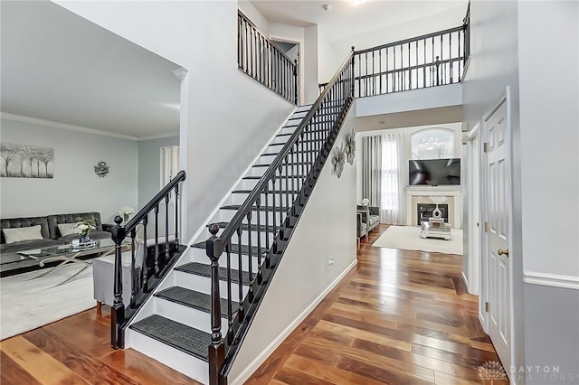 staircase with crown molding, a towering ceiling, and wood-type flooring