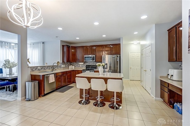 kitchen with appliances with stainless steel finishes, backsplash, a kitchen bar, a center island, and light tile patterned floors