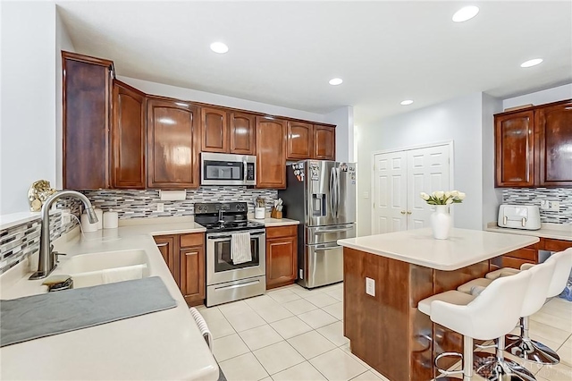 kitchen featuring sink, light tile patterned floors, a breakfast bar area, appliances with stainless steel finishes, and tasteful backsplash