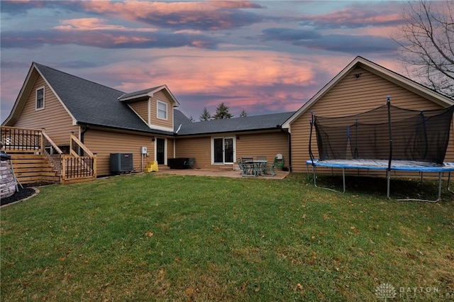 back house at dusk featuring a yard, a trampoline, central AC unit, and a patio area