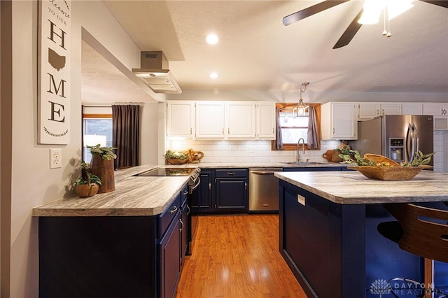 kitchen featuring blue cabinets, appliances with stainless steel finishes, tasteful backsplash, white cabinetry, and extractor fan