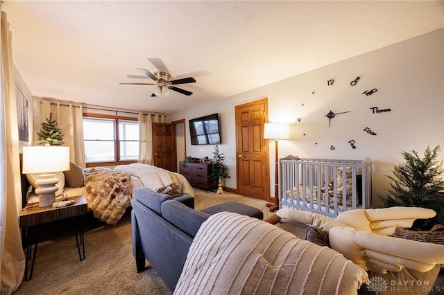 carpeted bedroom featuring ceiling fan and a crib