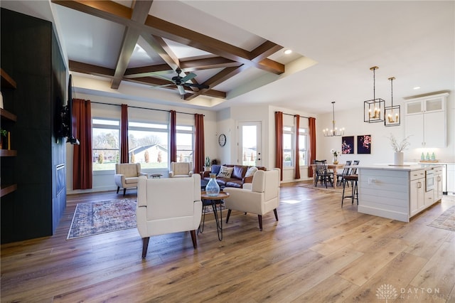 living room with beam ceiling, ceiling fan with notable chandelier, light hardwood / wood-style floors, and coffered ceiling