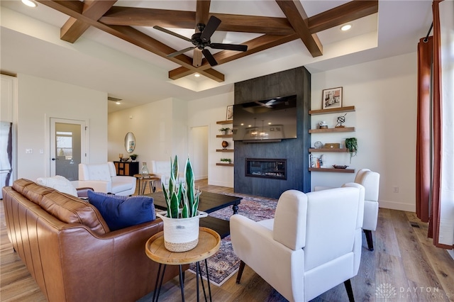 living room featuring coffered ceiling, ceiling fan, light wood-type flooring, a fireplace, and beamed ceiling