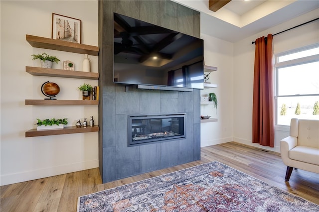 living room with beam ceiling, light wood-type flooring, and a tiled fireplace