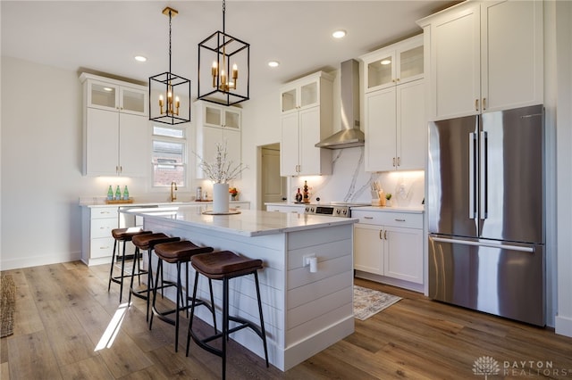 kitchen featuring white cabinetry, a kitchen island, wall chimney exhaust hood, and appliances with stainless steel finishes