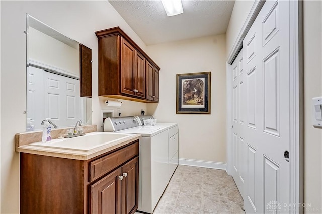 laundry area with a textured ceiling, washer and clothes dryer, cabinets, sink, and light tile patterned floors