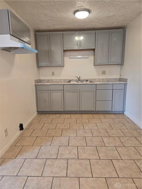 kitchen with gray cabinetry, sink, light tile patterned flooring, and a textured ceiling