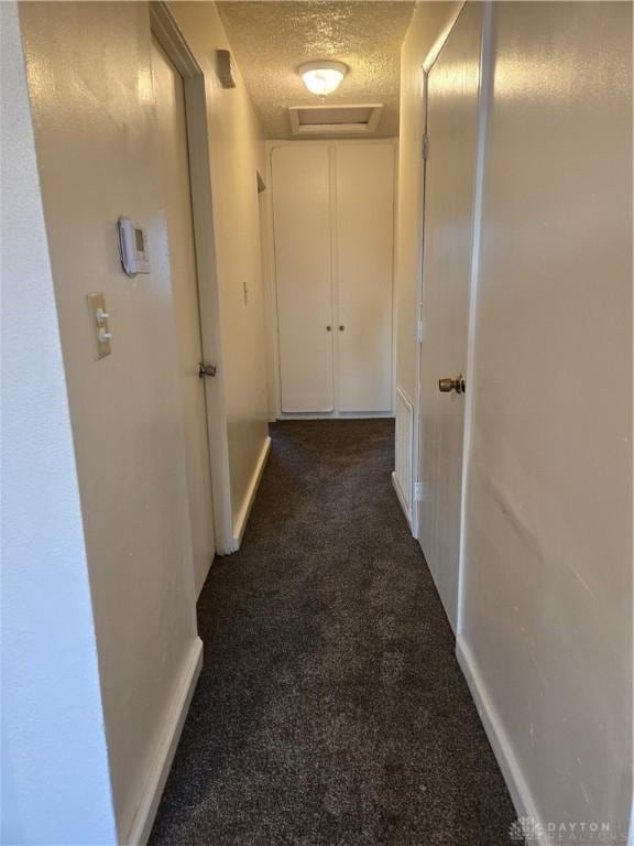 hallway with a textured ceiling and dark carpet