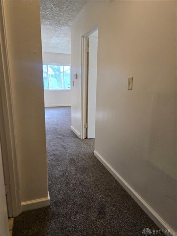 hall featuring a textured ceiling and dark carpet