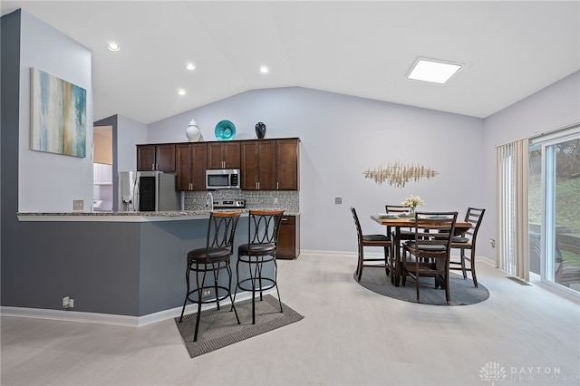 kitchen featuring dark brown cabinetry, stainless steel appliances, light stone counters, backsplash, and vaulted ceiling