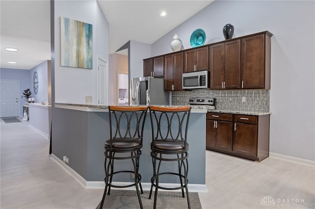 kitchen featuring decorative backsplash, dark brown cabinets, stainless steel appliances, and lofted ceiling